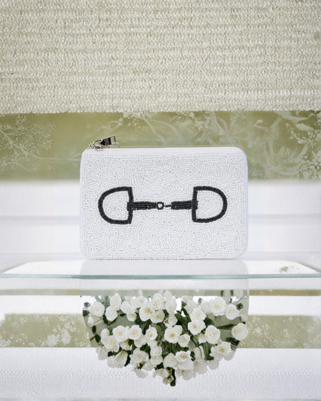 White clutch bag with black horse bit design on a white surface with flowers